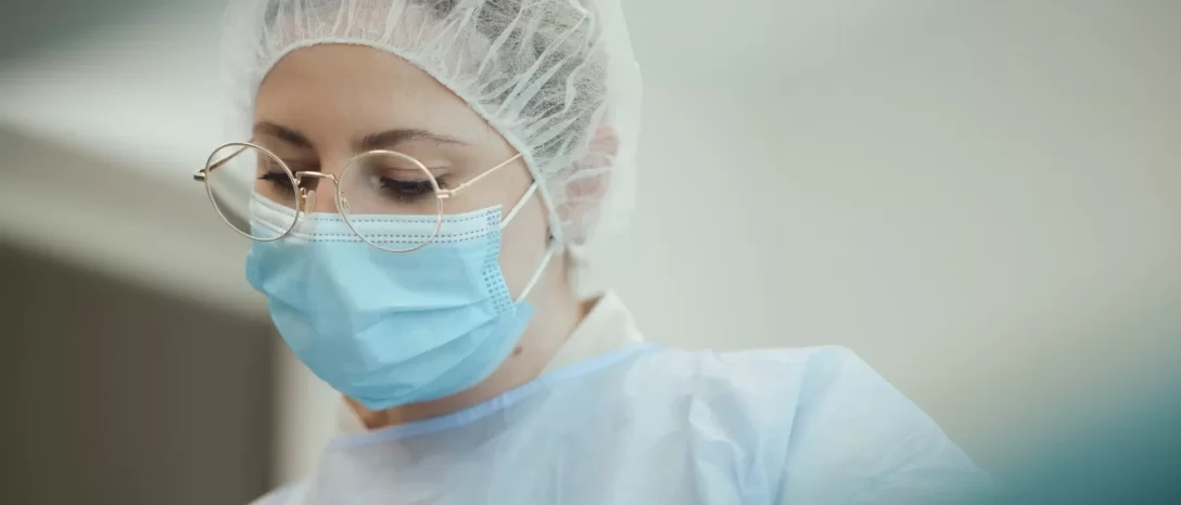 Gydytoja su apsaugine kauke, kepure ir akiniais susitelkusi atlieka medicininę procedūrą
