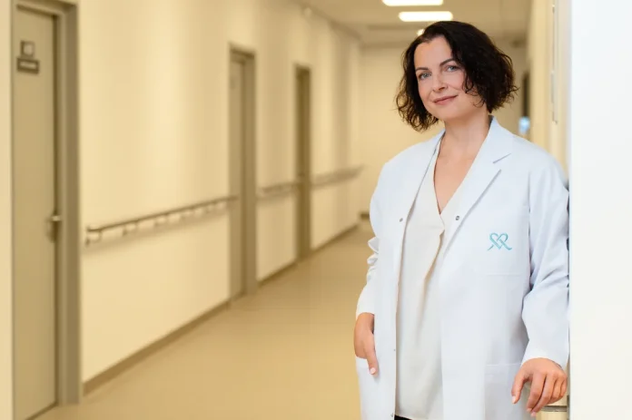 Moteris su baltu chalatu stovi klinikoje prie sienos 