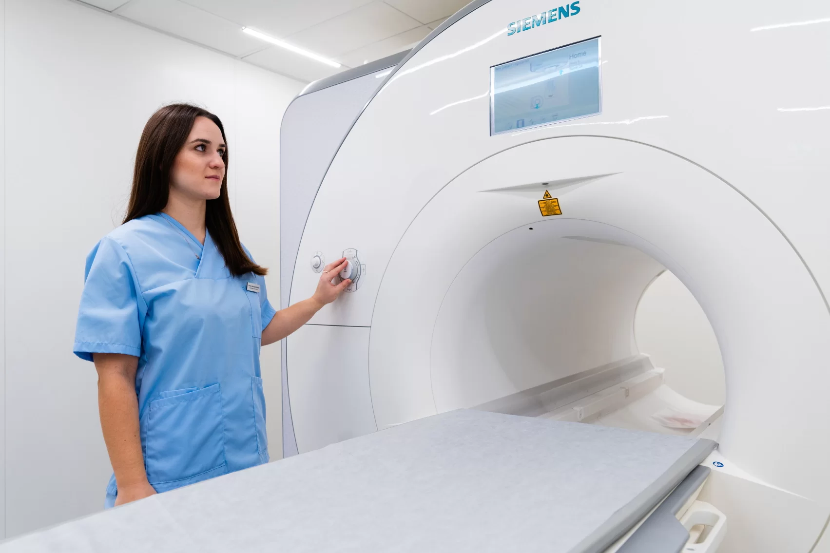 Medicinos darbuotoja prie magnetinio rezonanso tomografijos (MRT) aparato