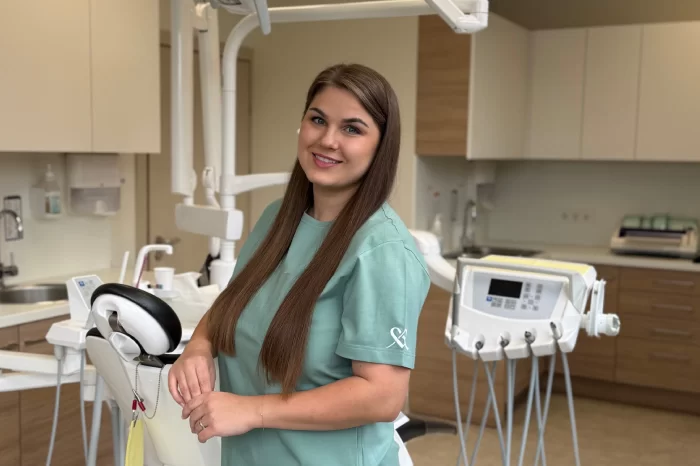 Odontologė stovi odontologijos kabinete prie paciento kėdės ir įrangos