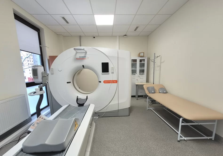 KT aparatas su paciento stalu ir apžiūros gultu radiologijos kabinete