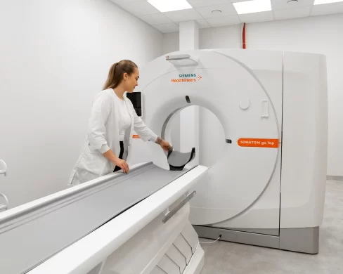 Medicinos darbuotoja ruošia kompiuterinės tomografijos aparatą tyrimui