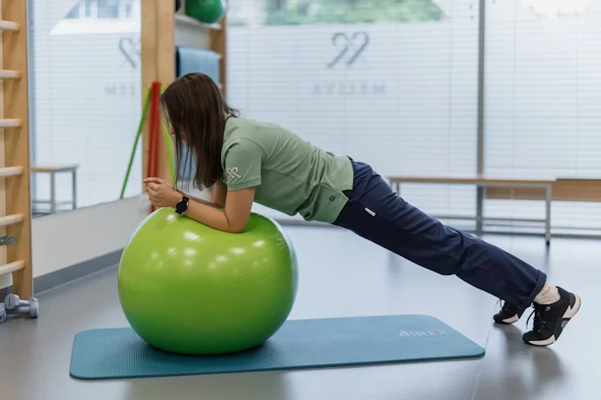 Kineziterapeutė atlieka atsispaudimų pratimą atsirėmusi į gimnastikos kamuolį