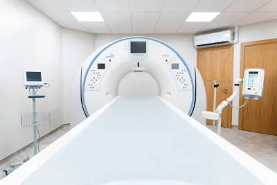 Kompiuterinės tomografijos (KT) aparatas iš priekio su paciento stalu