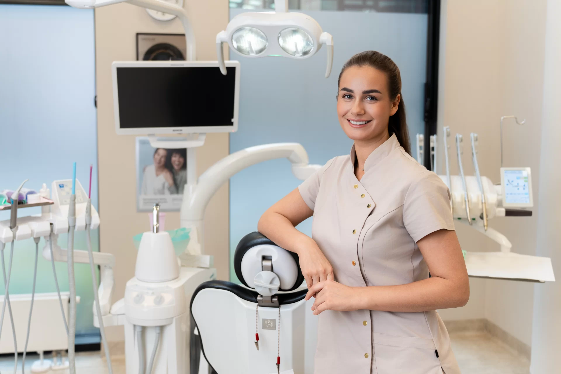 Odontologė stovi prie odontologinės kėdės ir įrangos kabinete